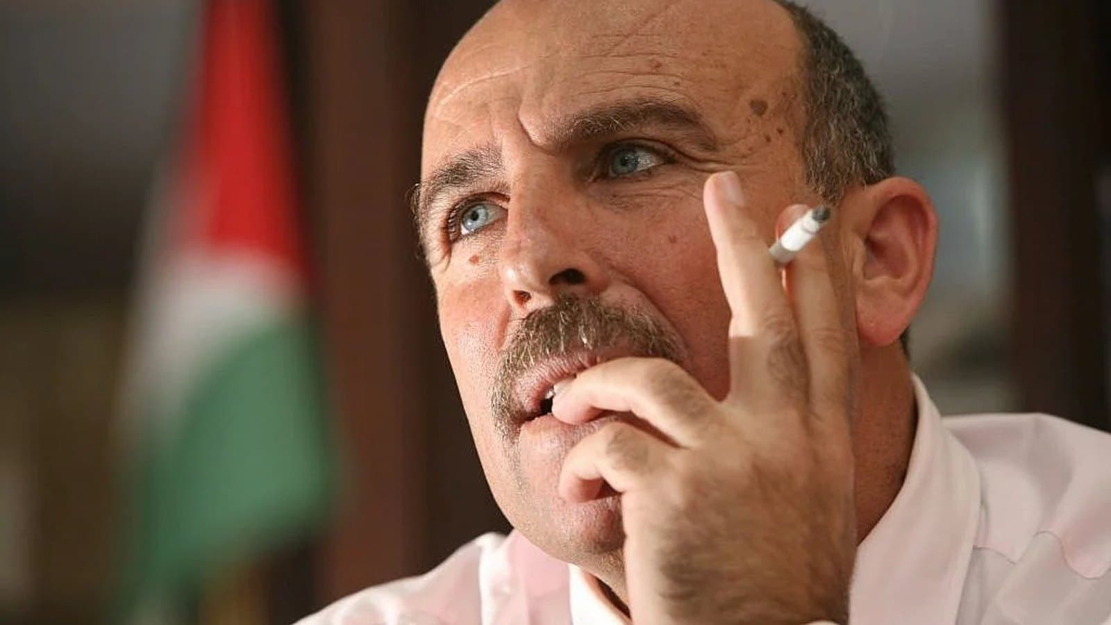Sufian Abu Zaida holding a cigarette while speaking, with a Palestinian flag behind him. File photograph.