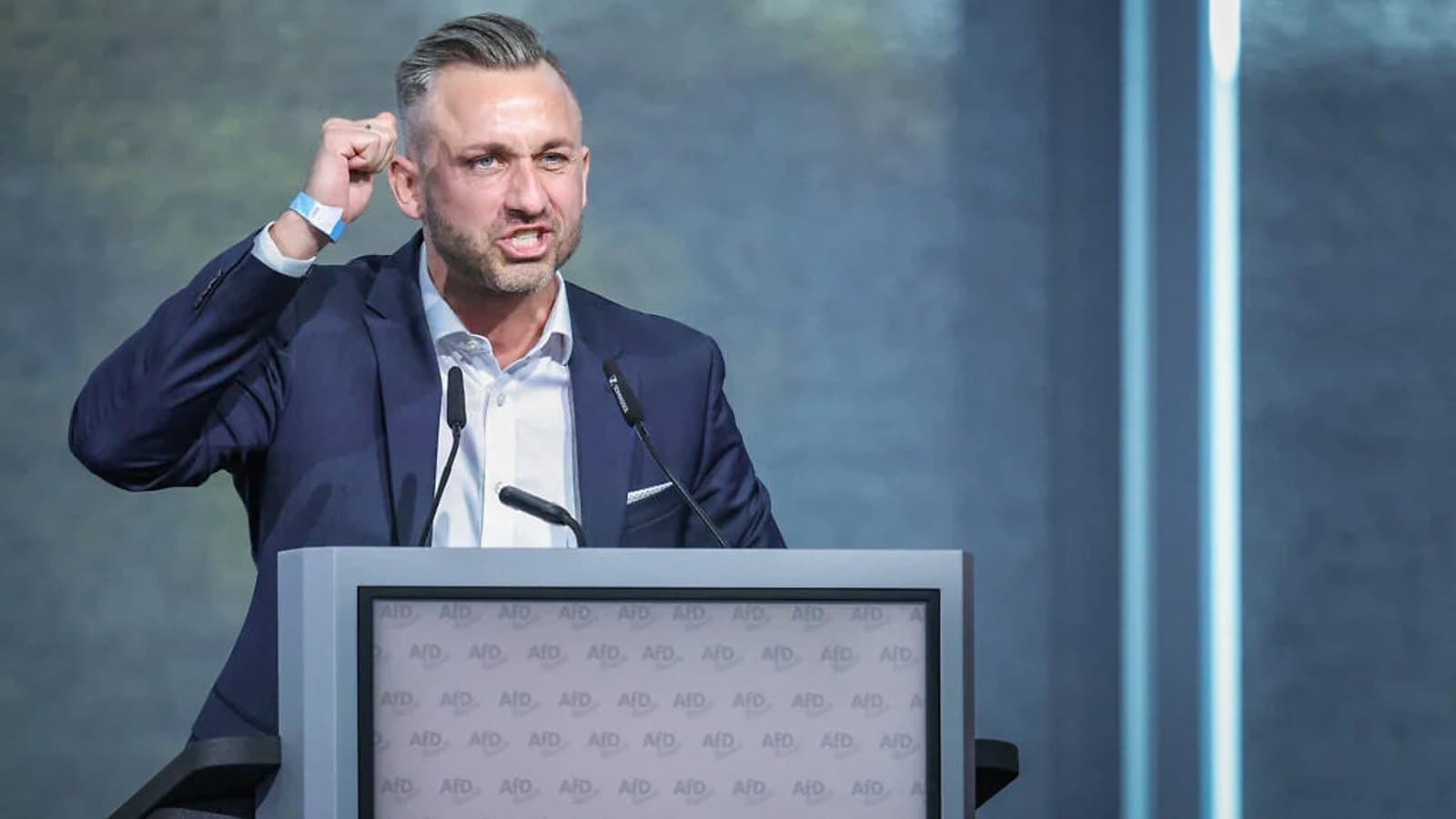 AfD top candidate Ulrich Siegmund gesturing while speaking at a podium branded with the party's logo. תצלום ארכיון.