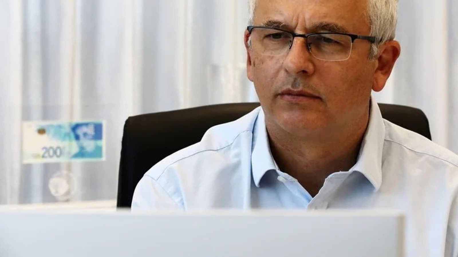A senior Bank of Israel official seated at a desk, with a 200 shekel banknote visible nearby. תצלום ארכיון.