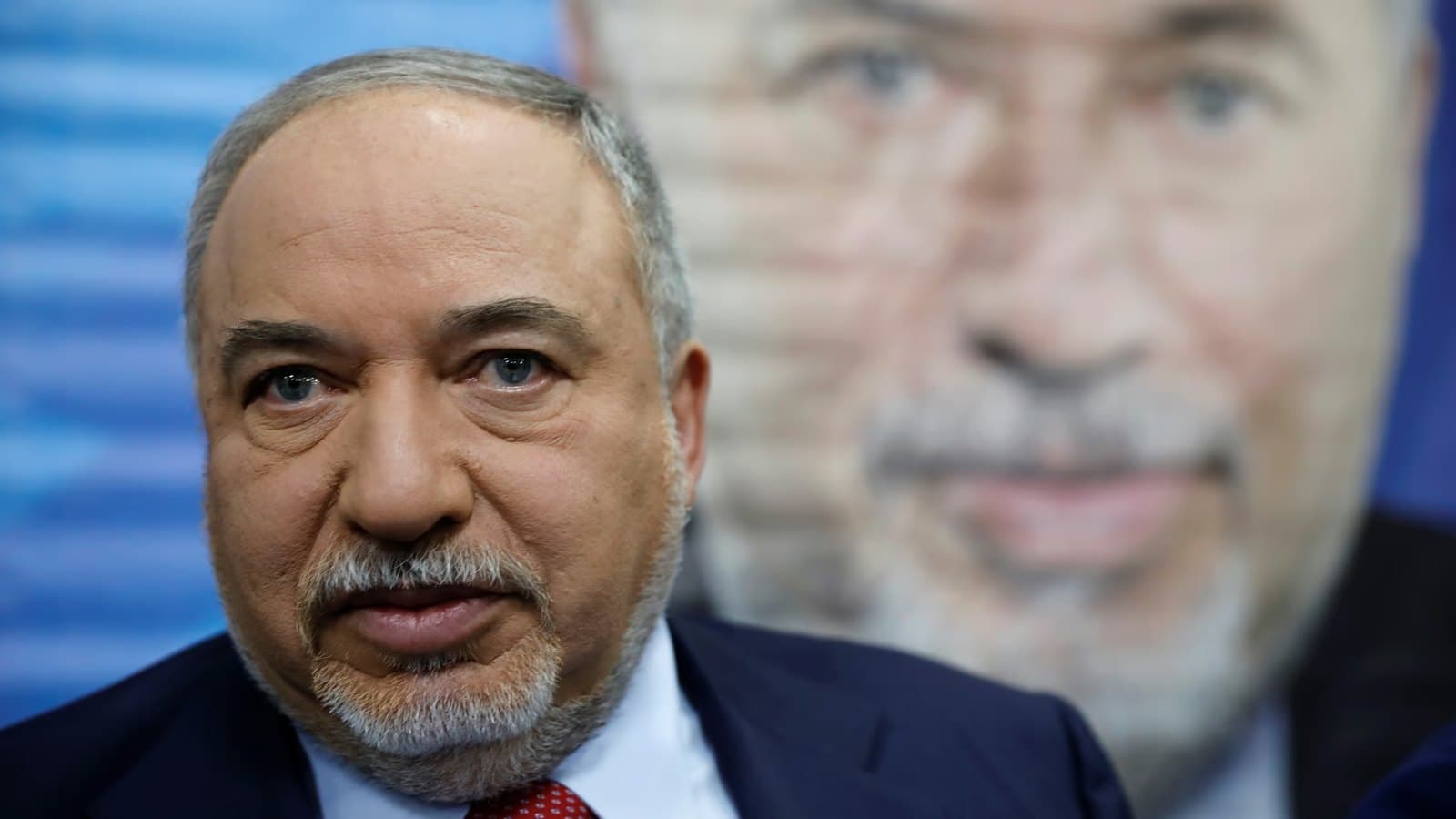 Avigdor Lieberman photographed in front of a blurred campaign poster bearing his own portrait.