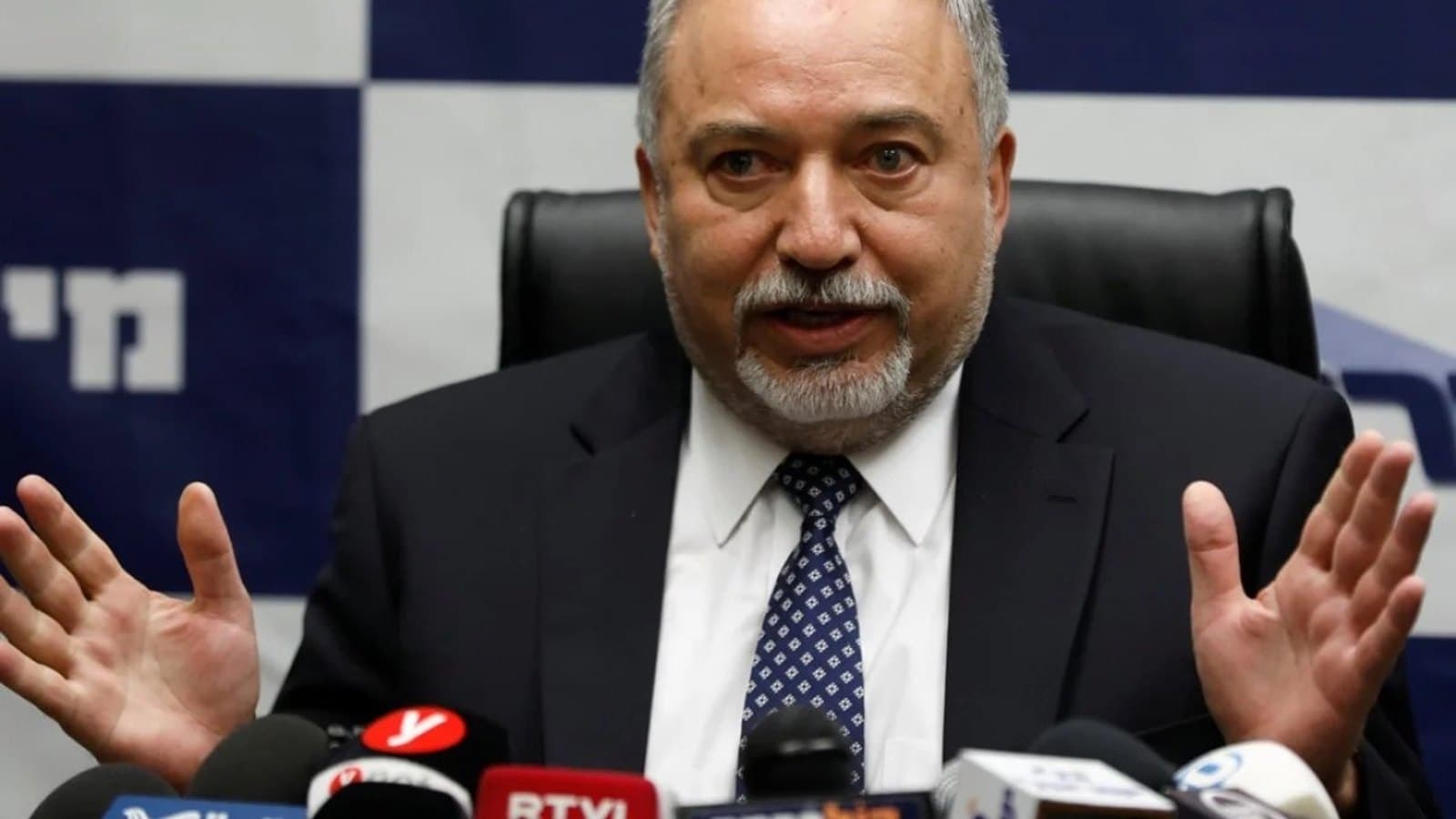 Avigdor Lieberman speaking with his hands raised at a press conference, with microphones in the foreground.