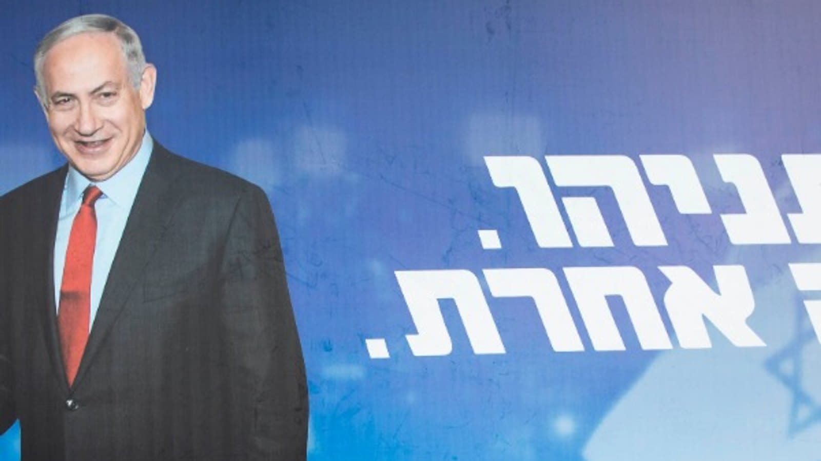 A woman in a yellow skirt walking past a large Netanyahu campaign billboard.