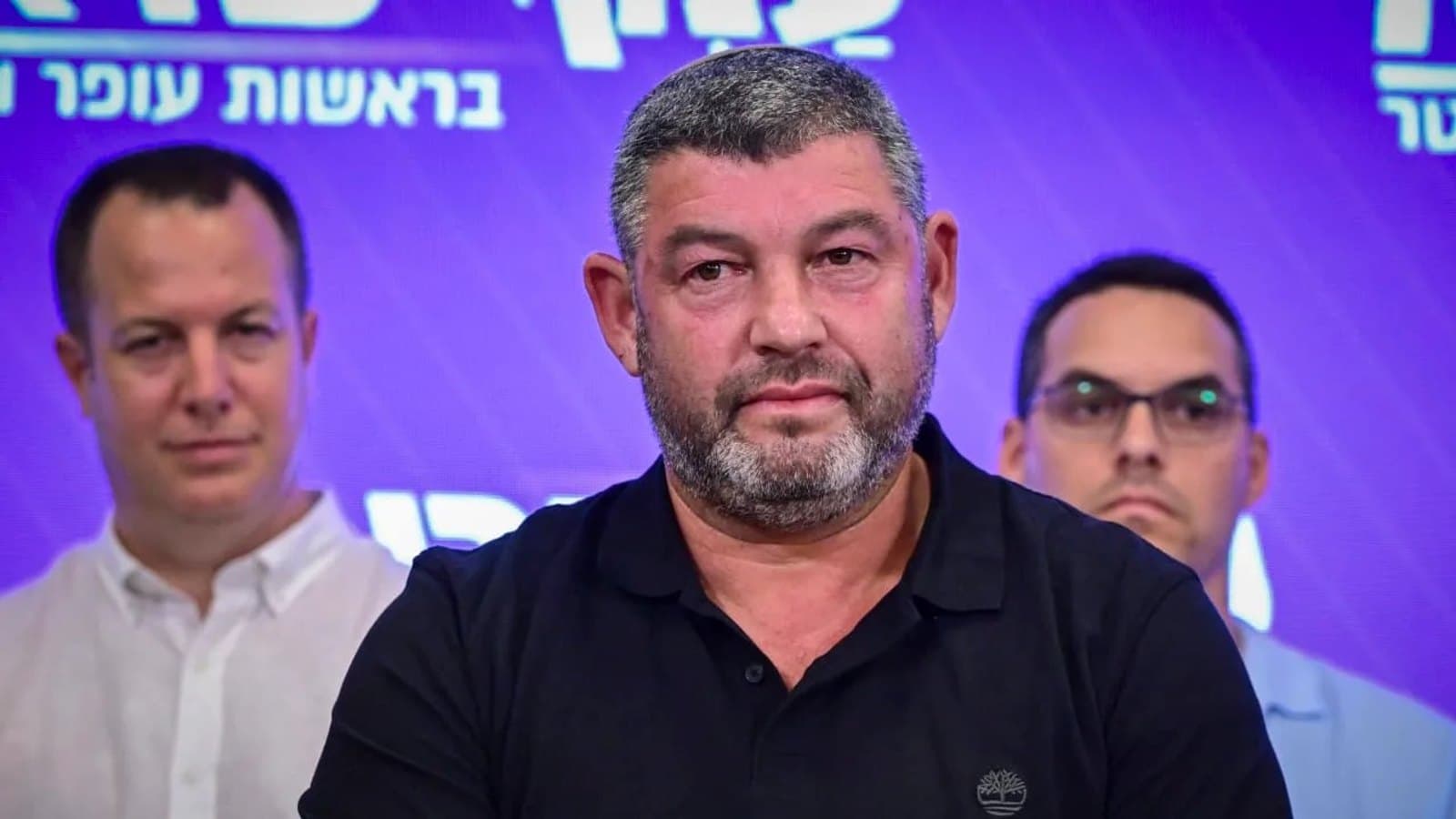 Ofer Winter standing before a campaign backdrop with two party colleagues beside him. תצלום ארכיון.