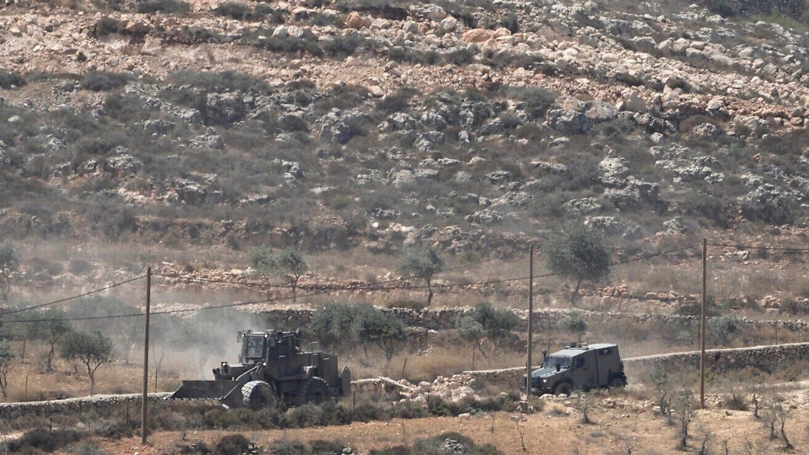 An army bulldozer and an armoured vehicle on a track through terraced hillside near Qusra.