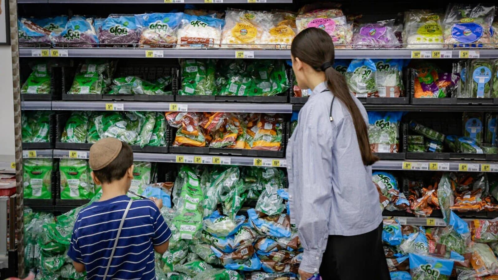 A mother and child looking at packaged produce on supermarket shelves.
