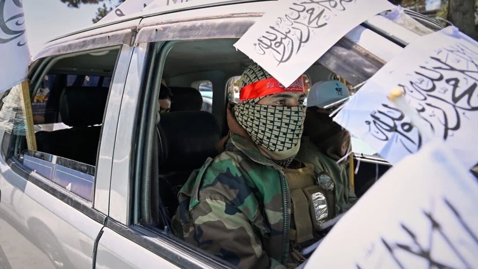 A masked Taliban fighter in a vehicle draped with Taliban flags during anniversary celebrations in Kabul.