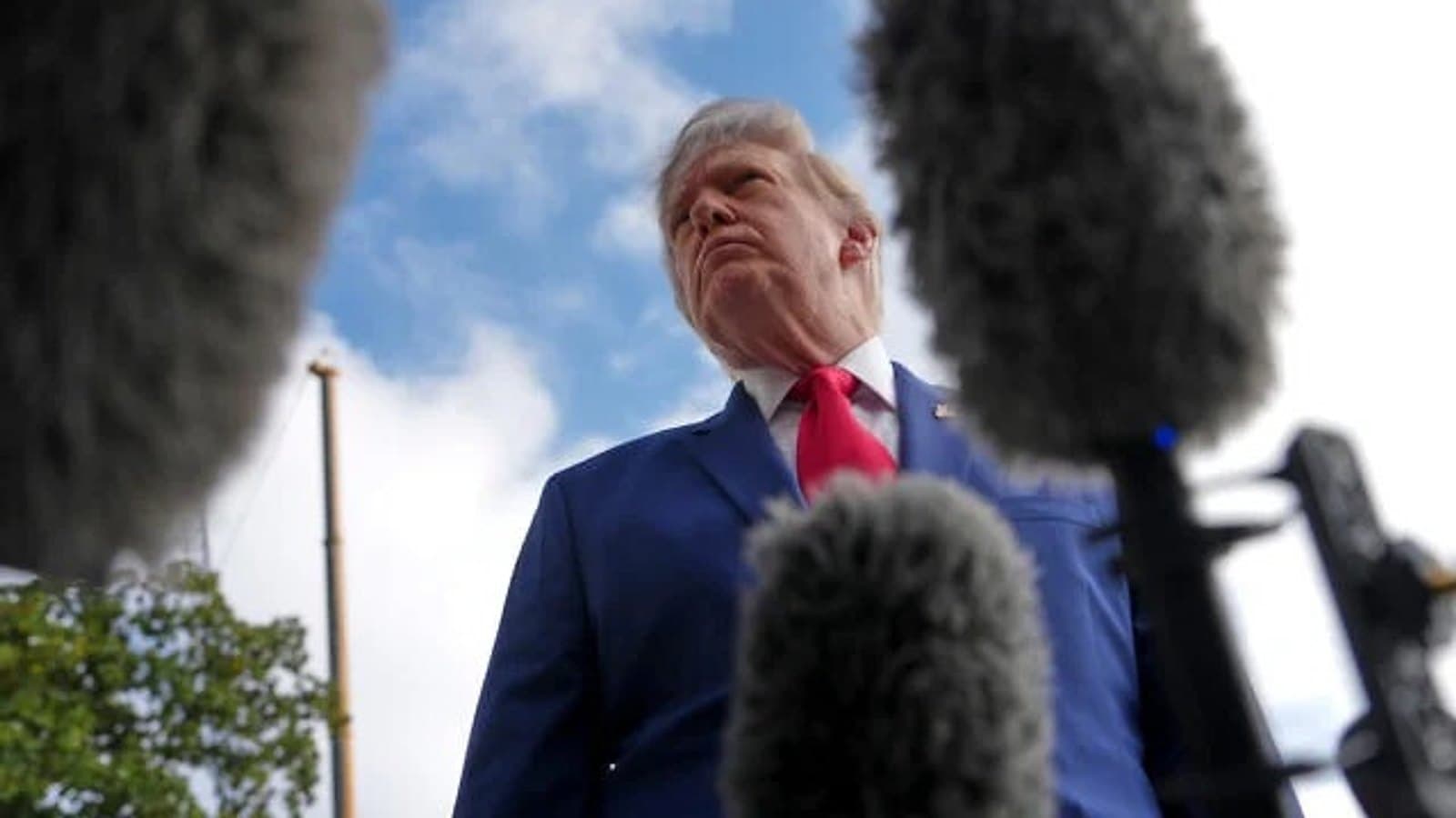President Trump pausing to speak with reporters outdoors, surrounded by microphones. תצלום ארכיון.