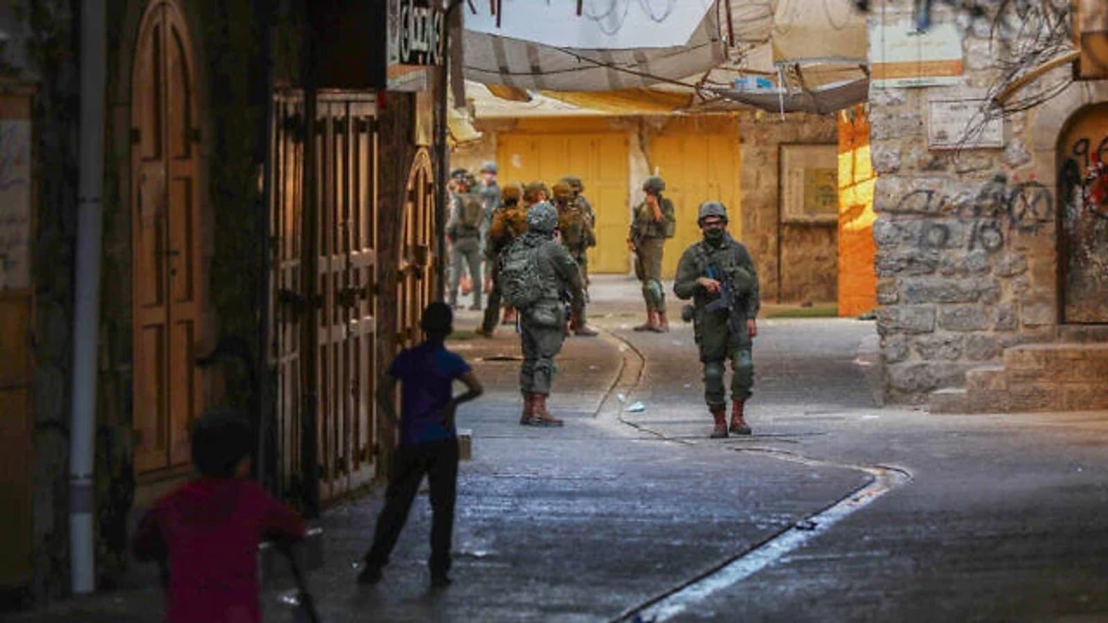 Israeli soldiers standing in a West Bank street as two children look on.