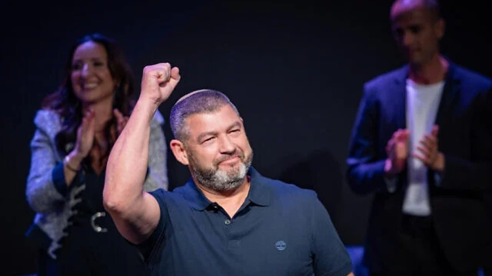 Ofer Winter raising a fist on stage as supporters applaud behind him.